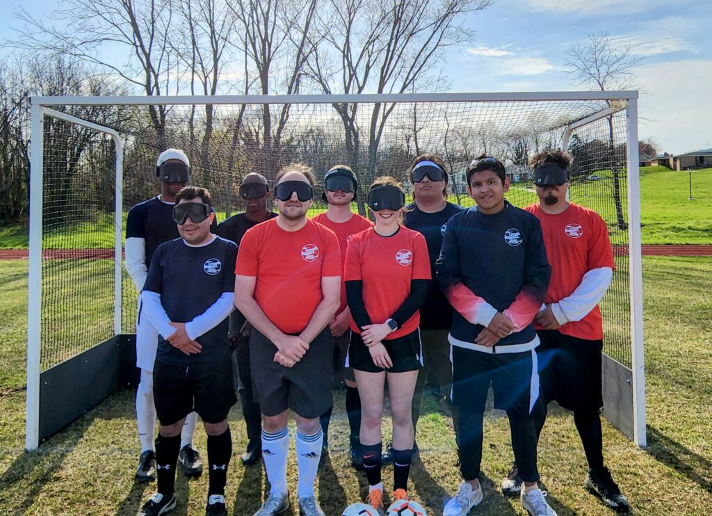 Athletes at the blind soccer camp pose for a group photo in front of a goal.