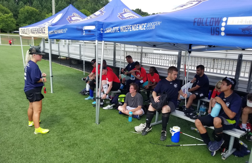 Coach Katie Smith stands in front of the camp participants who are seated under a canopy as she gives them direction.