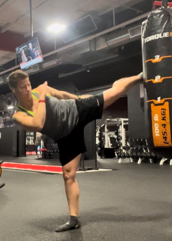 Asya in the gym kicking a punching bag with her left foot.