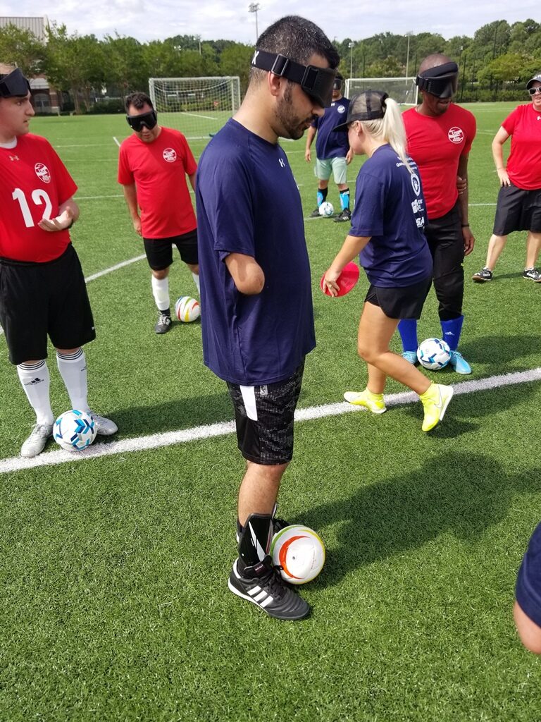 Ahmed Shareef stands with a soccer ball at his feet as coach Katie Smith directs other athletes in the background.