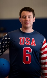 A photo of Calahan Young wearing a blue #6 USA jersey and holding a goalball under his right arm.