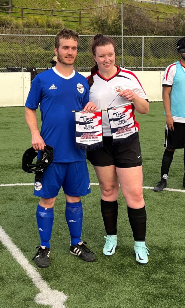 USA's Noah Beckman and Canada's Hillary Scanlon post for a photo at midfield while holding USA Blind Soccer pennants.