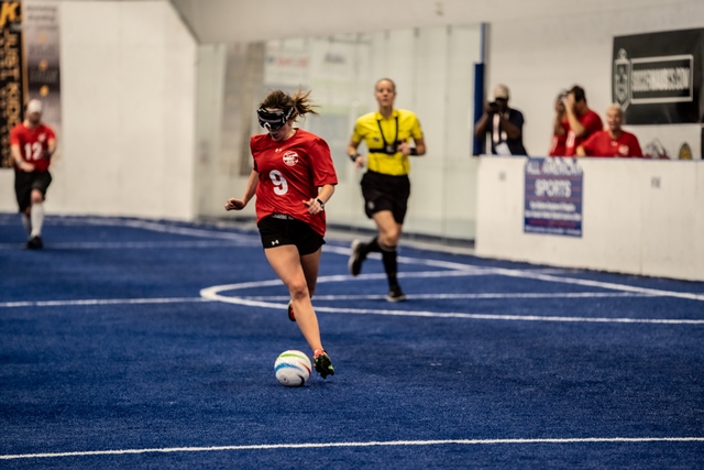 Bailey Martin dribbles a soccer ball down the field of blue turf as a referee trails the action.