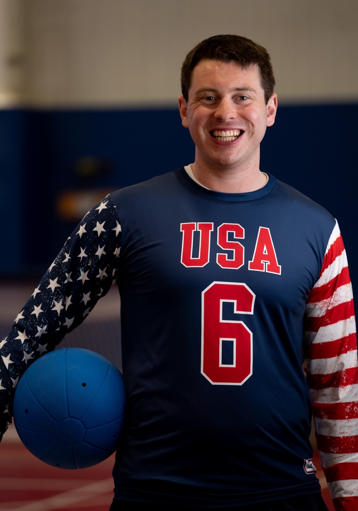 Calahan Young poses with a goalball under his arm while wearing his USA jersey with number 6 on the front