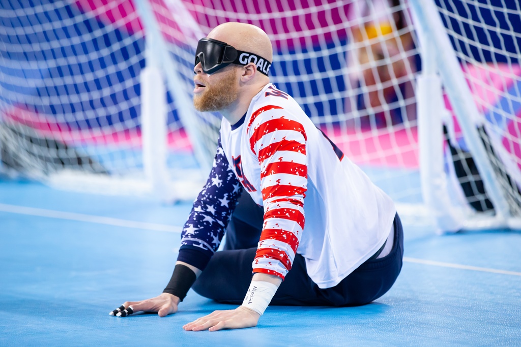 Daryl Walker sits on his left side in front of his goal during competition at the 2019 Parapan American Games in Lima, Peru. He is wearing dark eyeshades, a red, white and blue USA jersey, and tape on his fingers.