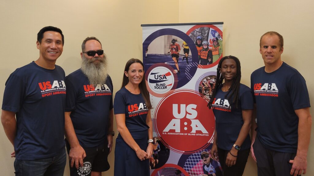 USABA endurance sport ambassadors Bryan Lam, Rob Sanchas, Shannon Houlihan, Jasmine Murrell and Kyle Coon pose next to a USABA banner wearing matching blue sport ambassador t-shirts.