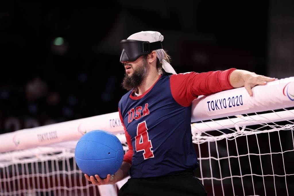 John Kusku holds a goalball in his right hand while he rests his left arm on the crossbar of the goal during the Tokyo 2020 Paralympic Games