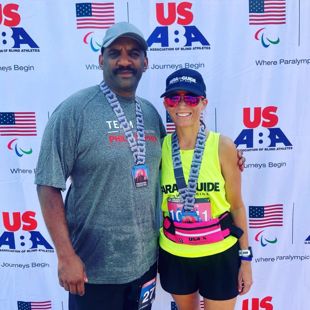 Ken Clausell poses with his guide and USABA Endurance Sport Ambassador Shannon Houlihan in front of a USABA backdrop