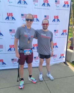 Kyle Coon and guide Greg Billington pose for a photo in front of a USABA backdrop after the race.