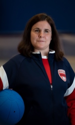 Libby Daugherty poses with a goalball under her right arm while wearing a blue USA Goalball National Team jacket.