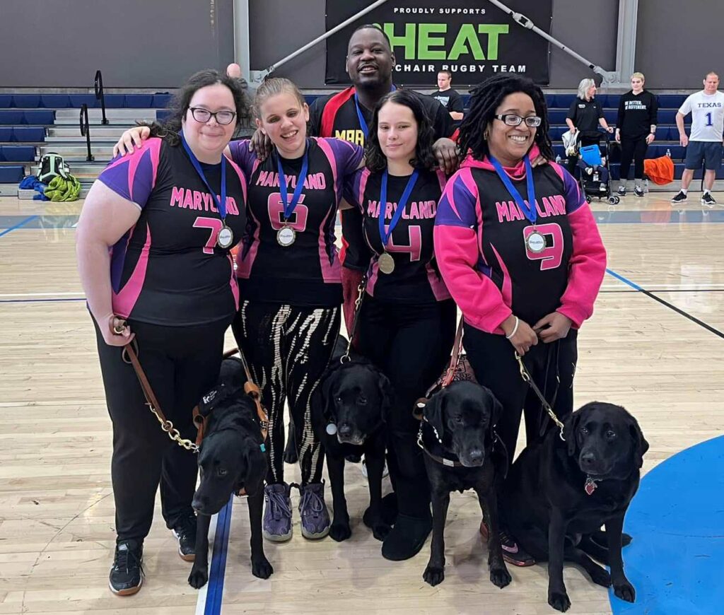 The Maryland Minks pose on the court with their gold medals and guide dogs.