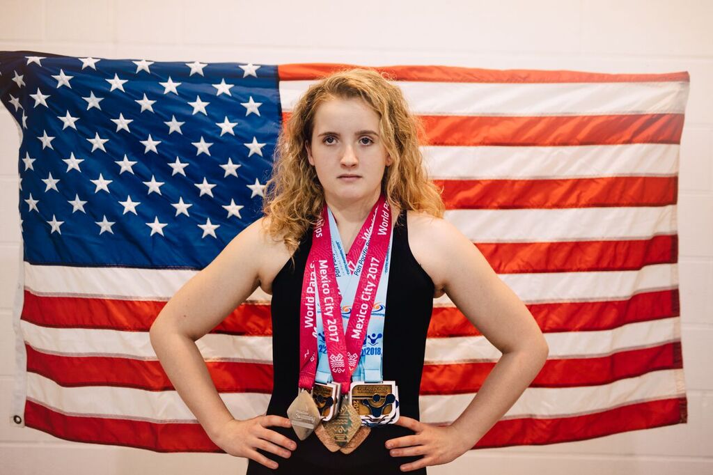 McClain Hermes poses with several medals around her neck and the American flag in the background