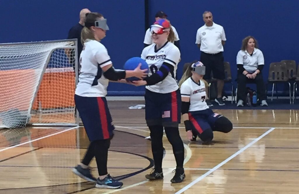 Mindy Cook (left) is handed a goalball by teammate Marybai Huking during a competition at Turnstone Center in Fort Wayne, Indiana.