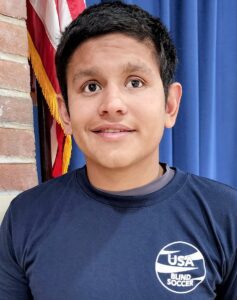 A headshot photo of Ricardo Castaneda wearing a blue USA Blind Soccer t-ahirt