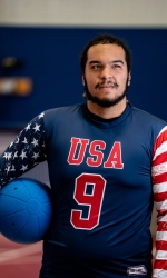 A headshot photo of Sean Walker wearing a blue #9 USA jersey and holding a goalball under his right arm.