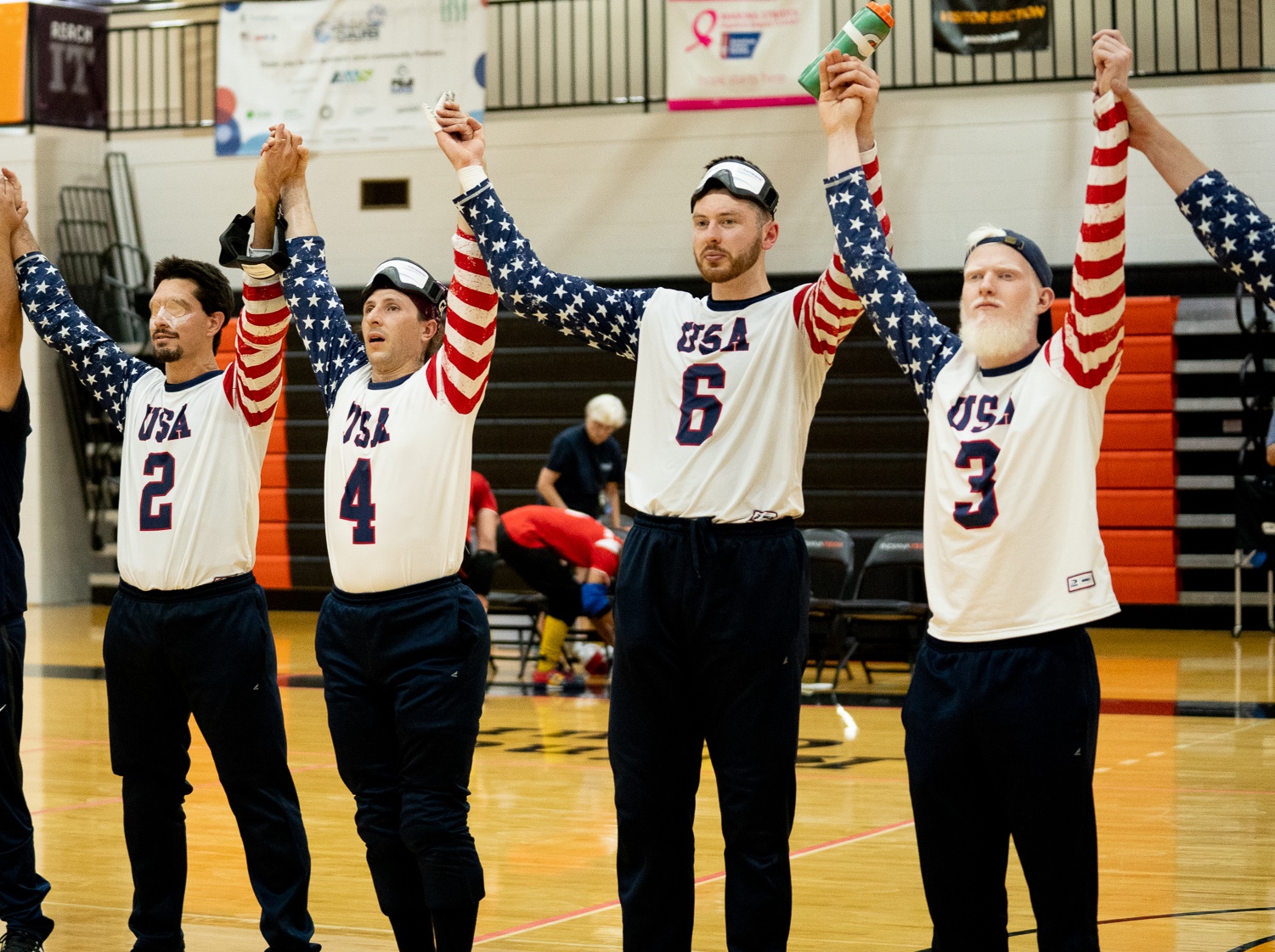 Wearing a white #3 USA jersey at far right, Josh Welborn raises his arms together with teammates Calahan Young, John Kusku and Tyler Merren after a win at the 2019 IBSA Goalball International Qualifier in Fort Wayne, Indiana.